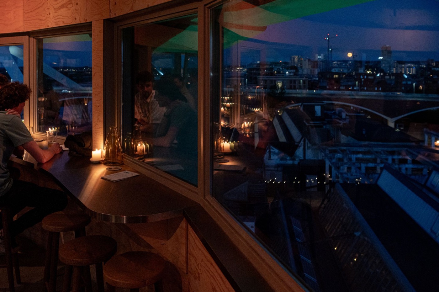 Aan de bar bij het raam, met kaarslicht en uitzicht over de stad bij avond