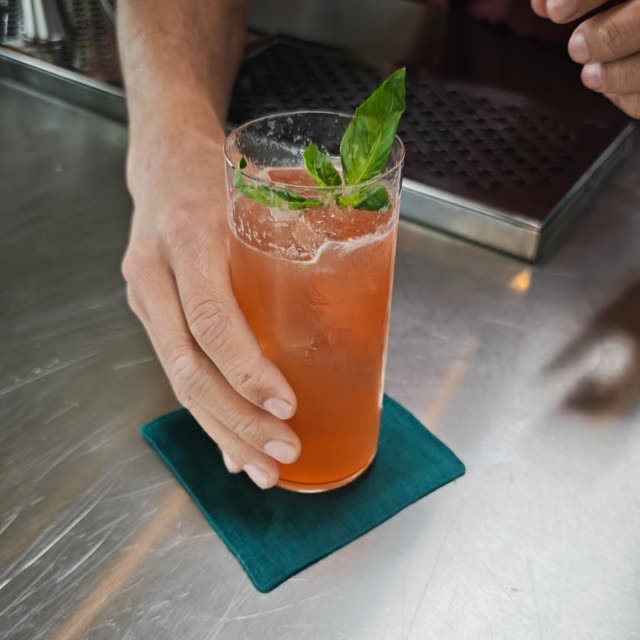 Een oranje cocktail met verse kruiden op een groene onderzetter
